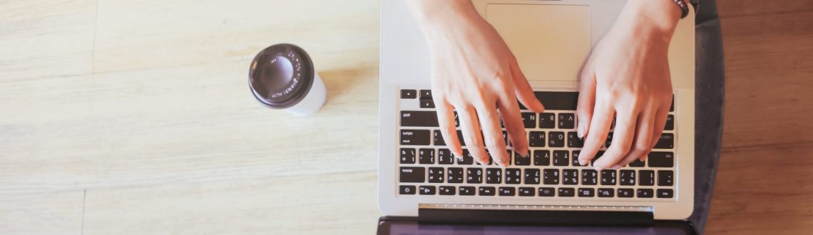 Top view of laptop in girl's hands sitting on a wooden floor with coffee